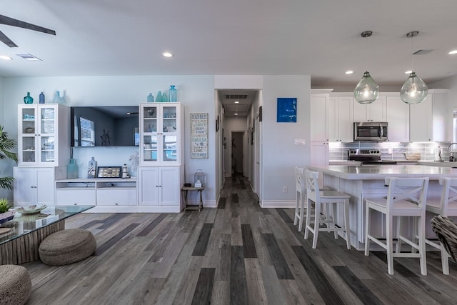 kitchen with dark hardwood / wood-style floors, hanging light fixtures, a breakfast bar area, white cabinetry, and appliances with stainless steel finishes