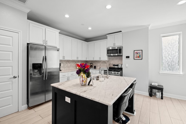 kitchen featuring appliances with stainless steel finishes, tasteful backsplash, an island with sink, white cabinetry, and light stone countertops