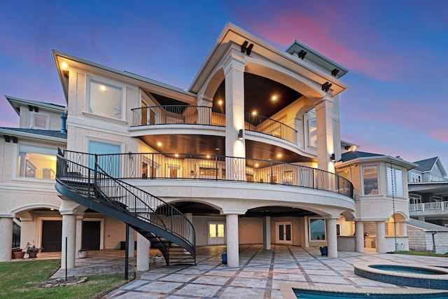 back house at dusk with a balcony and a patio