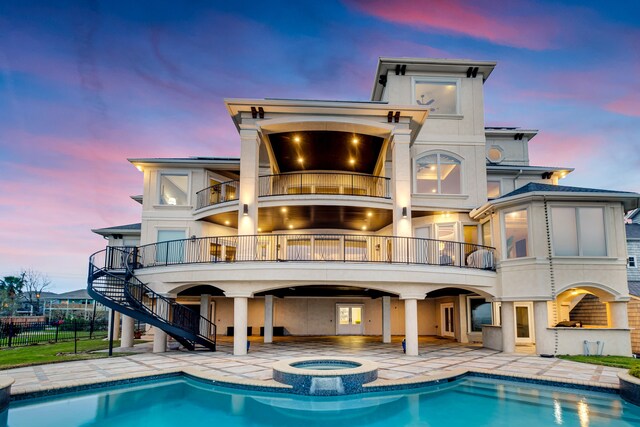 back house at dusk featuring a balcony, a patio area, and a swimming pool with hot tub