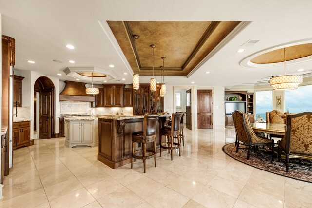 kitchen featuring decorative light fixtures, a kitchen island, a tray ceiling, and custom range hood