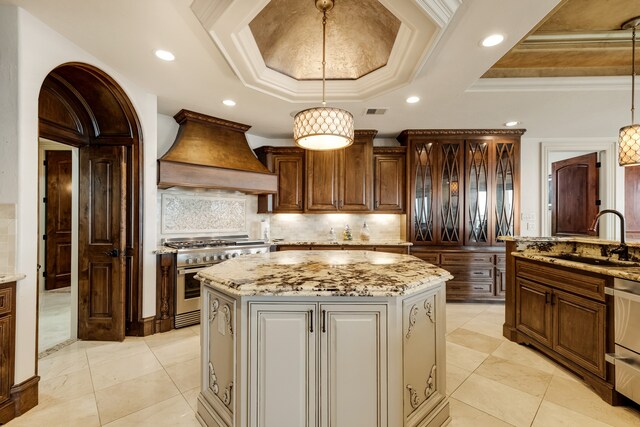 kitchen featuring an island with sink, a tray ceiling, double oven range, hanging light fixtures, and custom range hood