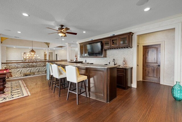 kitchen with pendant lighting, a breakfast bar, ceiling fan with notable chandelier, dark hardwood / wood-style flooring, and dark brown cabinets