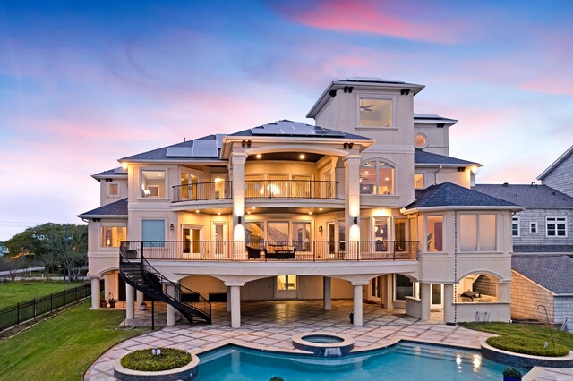 back house at dusk with a balcony, solar panels, a lawn, a fenced in pool, and a patio