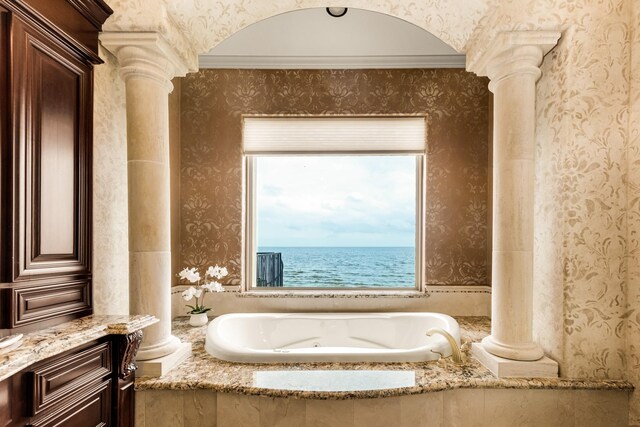 bathroom with a water view, decorative columns, ornamental molding, and a relaxing tiled bath