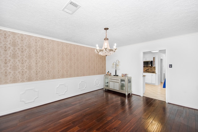 unfurnished room featuring an inviting chandelier, a textured ceiling, ornamental molding, and dark wood-type flooring