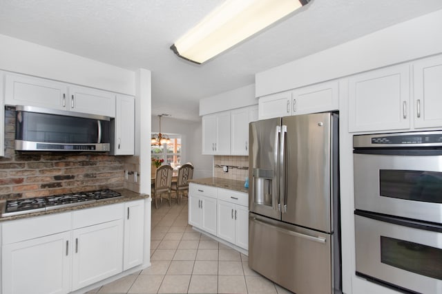 kitchen featuring dark stone counters, an inviting chandelier, white cabinetry, stainless steel appliances, and backsplash