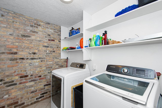 washroom featuring a textured ceiling, brick wall, tile floors, and washing machine and clothes dryer