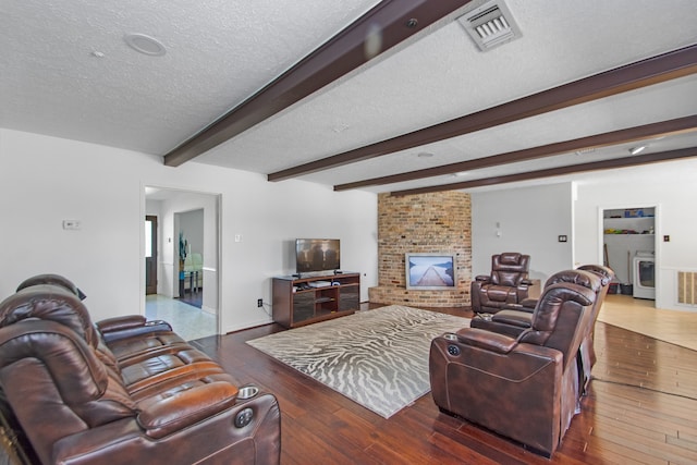 living room featuring a brick fireplace, dark wood-type flooring, a textured ceiling, and beamed ceiling