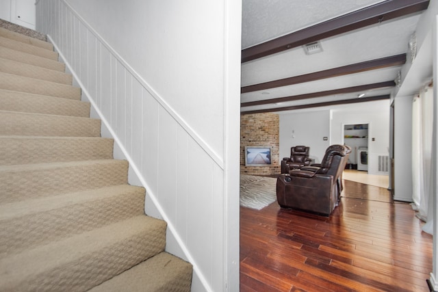 stairway with brick wall, a fireplace, dark wood-type flooring, and beamed ceiling