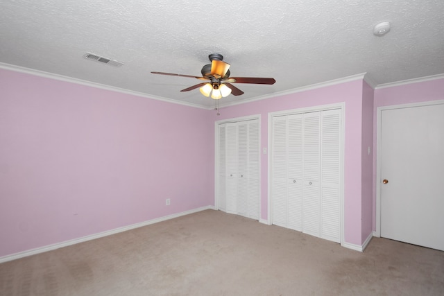 unfurnished bedroom with ornamental molding, light colored carpet, ceiling fan, and multiple closets