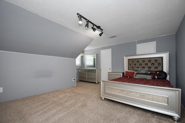 bedroom with lofted ceiling, light carpet, a textured ceiling, and track lighting