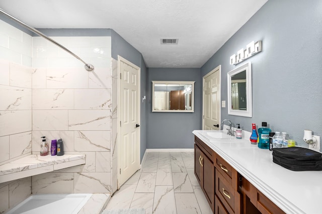 bathroom featuring tiled shower, a textured ceiling, and vanity