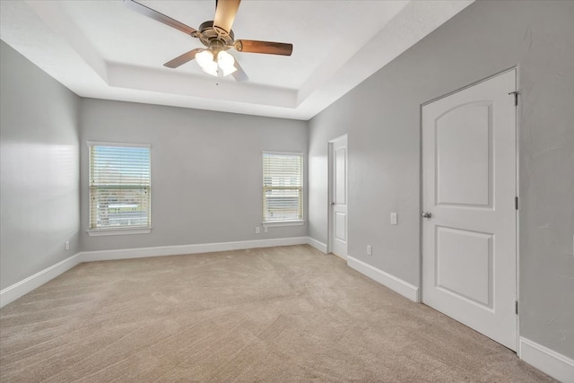 carpeted spare room with ceiling fan, a tray ceiling, and a healthy amount of sunlight