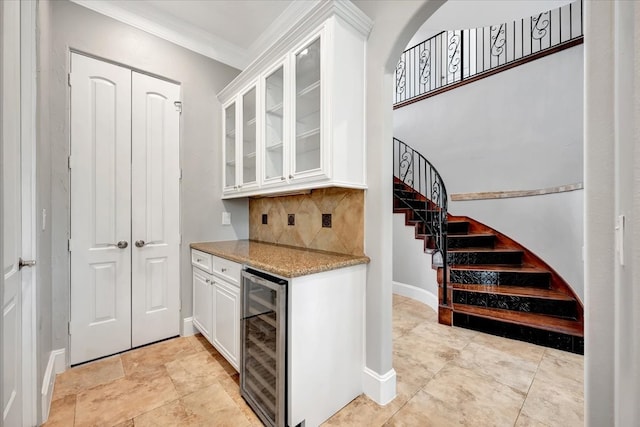 kitchen with light stone counters, tasteful backsplash, wine cooler, white cabinets, and crown molding