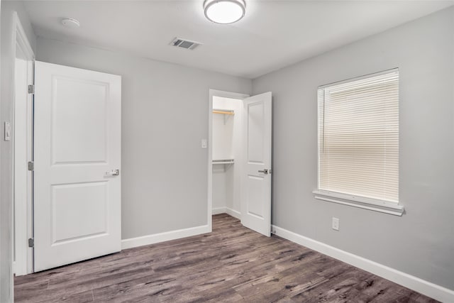 unfurnished bedroom with a closet, a walk in closet, and dark hardwood / wood-style flooring