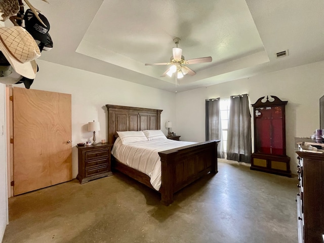 bedroom with concrete floors, a tray ceiling, and ceiling fan