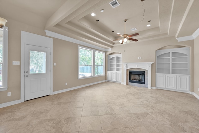 unfurnished living room featuring built in features, a tray ceiling, a tile fireplace, ceiling fan, and light tile patterned floors