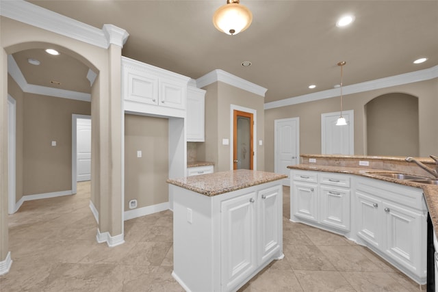 kitchen featuring light stone countertops, a kitchen island, hanging light fixtures, white cabinets, and ornamental molding