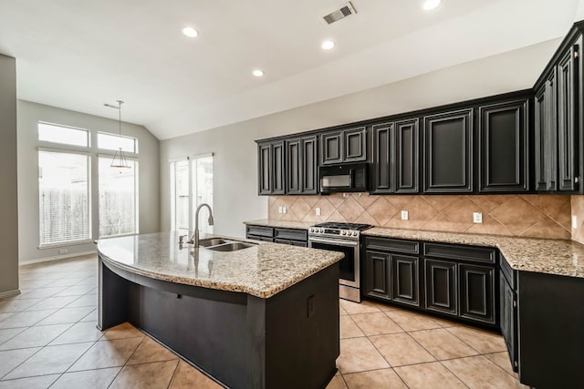 kitchen with stainless steel gas stove, light stone counters, backsplash, sink, and a center island with sink