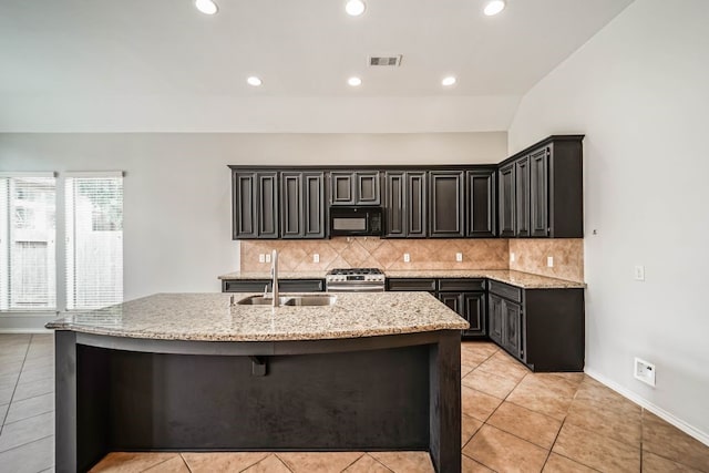 kitchen with light tile flooring, stainless steel range, a kitchen island with sink, and sink