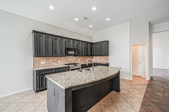 kitchen featuring an island with sink, sink, light stone counters, high end range, and tasteful backsplash