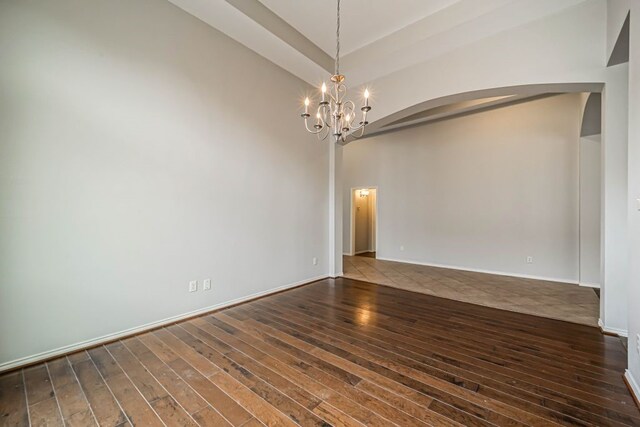 unfurnished room featuring a raised ceiling, a notable chandelier, a high ceiling, and dark hardwood / wood-style floors