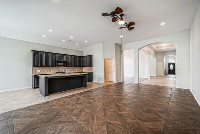 kitchen featuring dark parquet floors, tasteful backsplash, an island with sink, ceiling fan, and a breakfast bar area