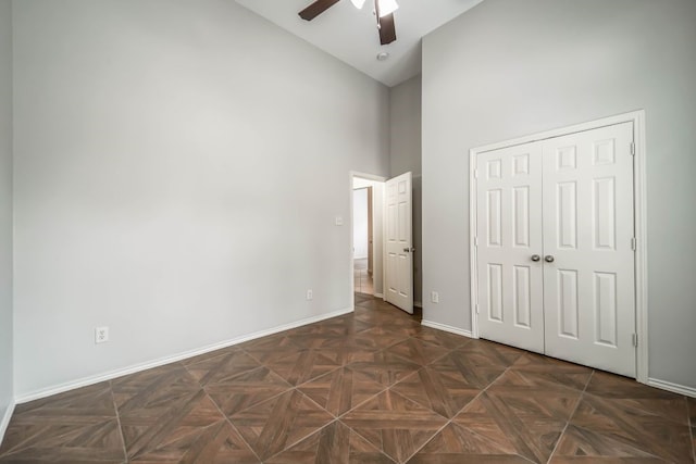 unfurnished bedroom with high vaulted ceiling, a closet, ceiling fan, and dark parquet flooring