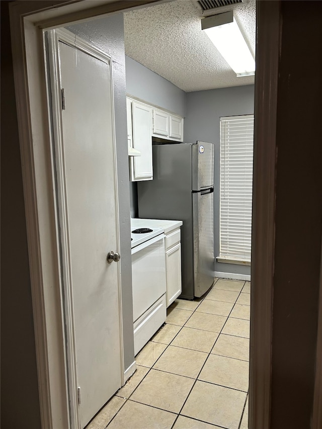 kitchen with electric range, light tile floors, a textured ceiling, white cabinetry, and range hood