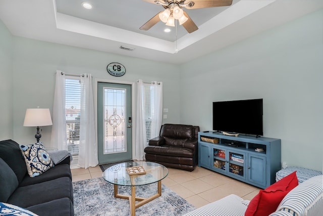 living room with a raised ceiling, ceiling fan, and light tile floors