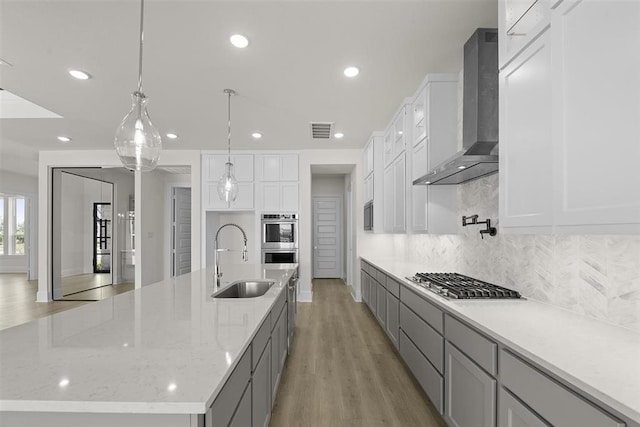 kitchen featuring a large island with sink, wall chimney exhaust hood, stainless steel appliances, sink, and pendant lighting