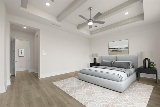 bedroom with a raised ceiling, wood-type flooring, and ceiling fan