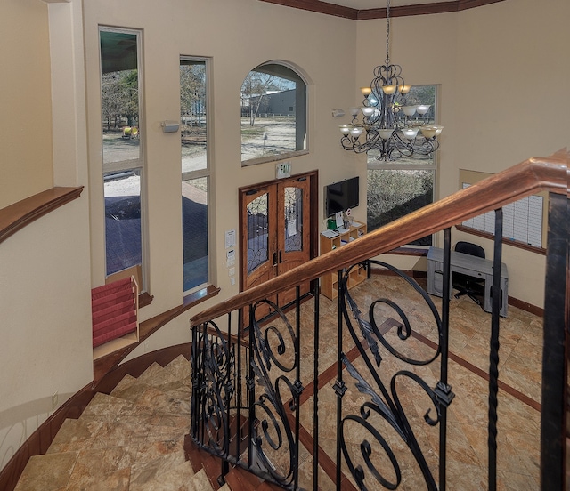 stairway with ornamental molding, french doors, and an inviting chandelier