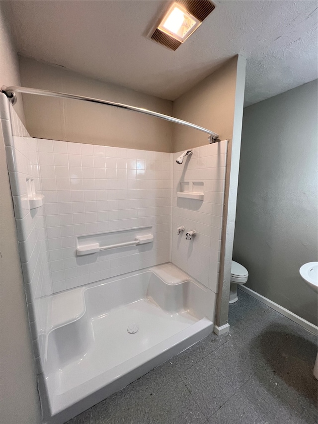 bathroom featuring tiled shower / bath, tile floors, toilet, and a textured ceiling