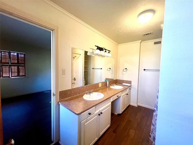 bathroom with crown molding, oversized vanity, wood-type flooring, and dual sinks