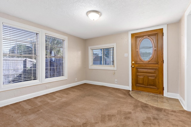 foyer entrance with a textured ceiling and light colored carpet