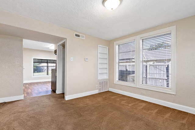 spare room featuring a wealth of natural light, dark colored carpet, and a textured ceiling