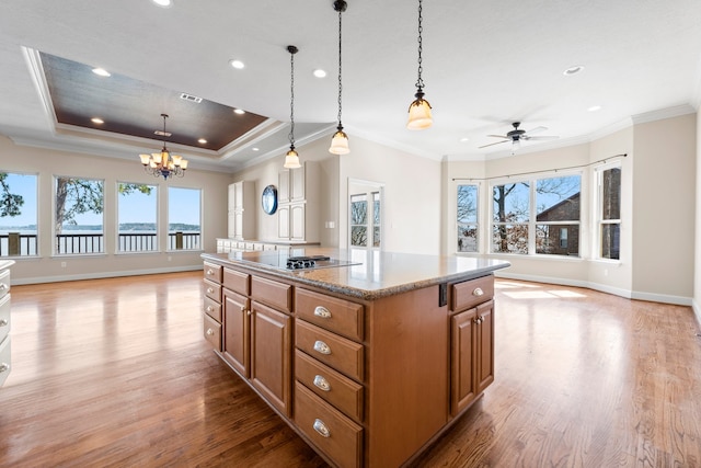 kitchen featuring a center island, light wood-type flooring, ceiling fan with notable chandelier, hanging light fixtures, and a raised ceiling