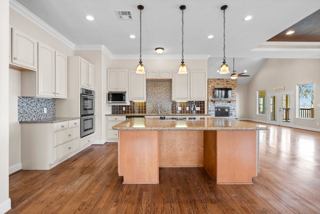 kitchen with decorative light fixtures, appliances with stainless steel finishes, a kitchen island, dark hardwood / wood-style floors, and light stone countertops