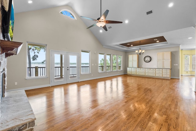 unfurnished living room with light hardwood / wood-style floors, a towering ceiling, a fireplace, ceiling fan with notable chandelier, and a tray ceiling