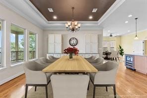 dining area with a notable chandelier, light hardwood / wood-style floors, a tray ceiling, and ornamental molding