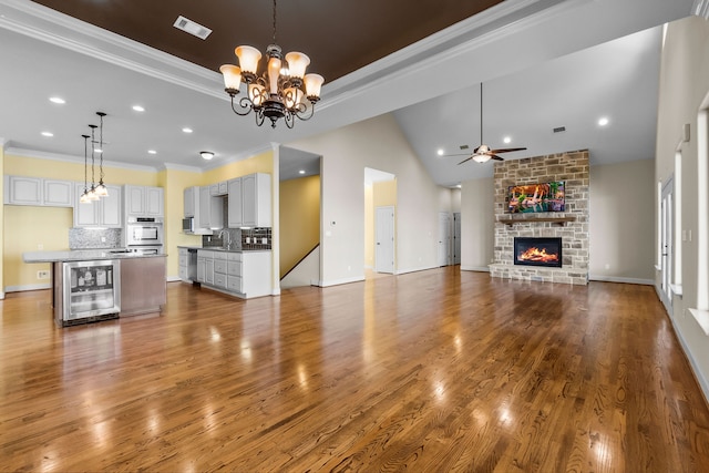 unfurnished living room featuring a brick fireplace, beverage cooler, hardwood / wood-style floors, and ceiling fan with notable chandelier