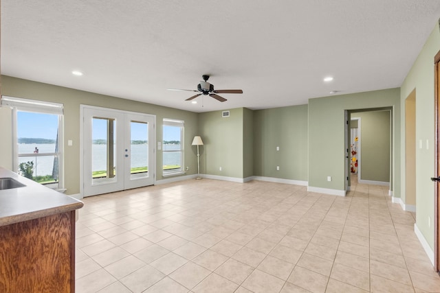 unfurnished living room with a water view, light tile floors, ceiling fan, and french doors