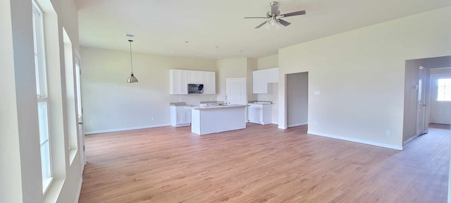 interior space featuring ceiling fan, hanging light fixtures, hardwood / wood-style floors, white cabinets, and a center island with sink