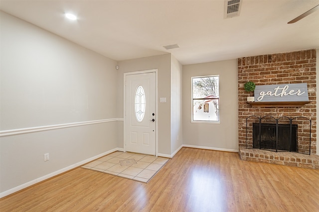 foyer with a fireplace, light hardwood / wood-style flooring, brick wall, and ceiling fan