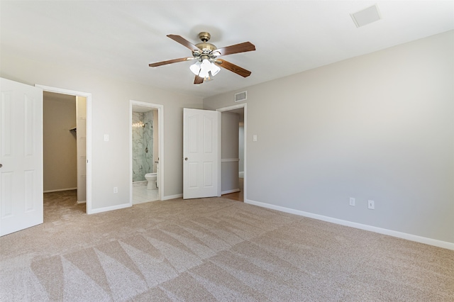 unfurnished bedroom with ceiling fan, a walk in closet, light carpet, a closet, and ensuite bath