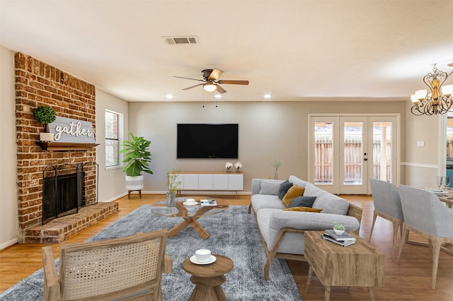 living room with a fireplace, wood-type flooring, ceiling fan with notable chandelier, brick wall, and french doors