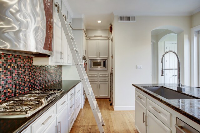 kitchen featuring backsplash, light hardwood / wood-style flooring, appliances with stainless steel finishes, dark stone countertops, and sink