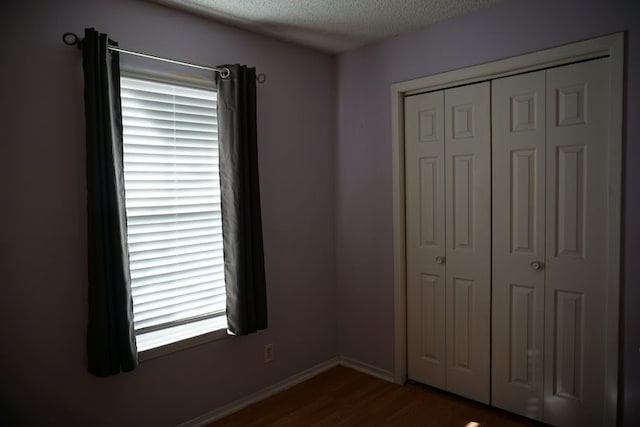 unfurnished bedroom with a closet, a textured ceiling, multiple windows, and dark hardwood / wood-style flooring